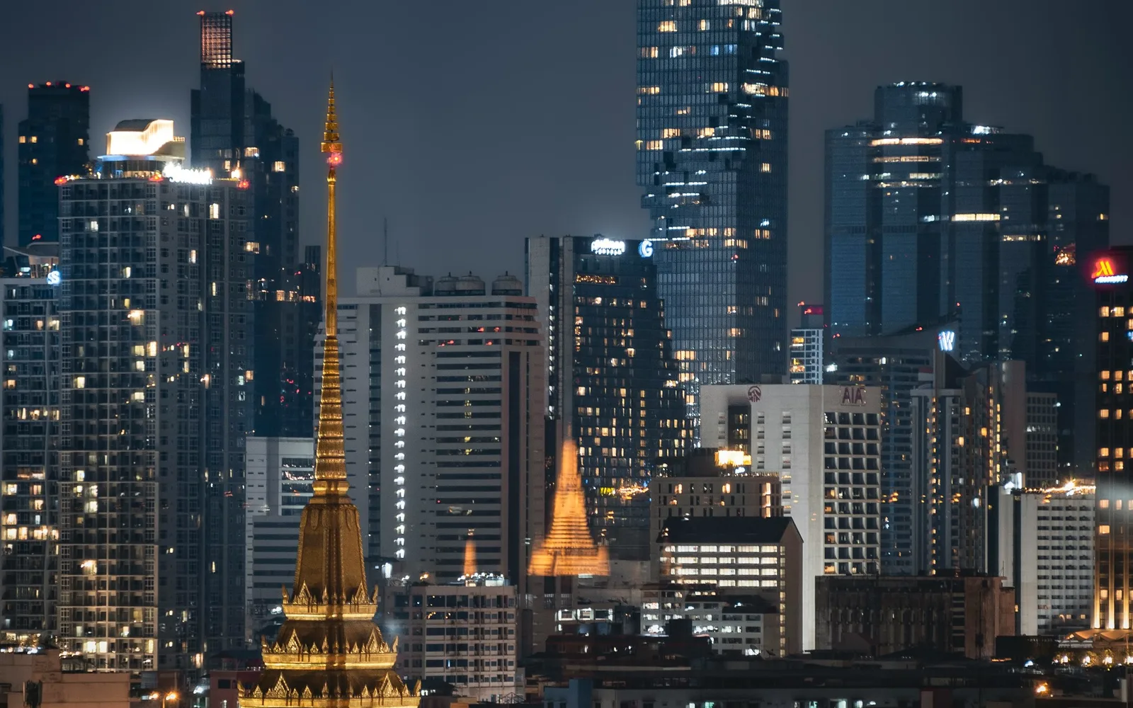 Bangkoks skyline om natten med gyllene tempelspiror och MahaNakhon-tornet